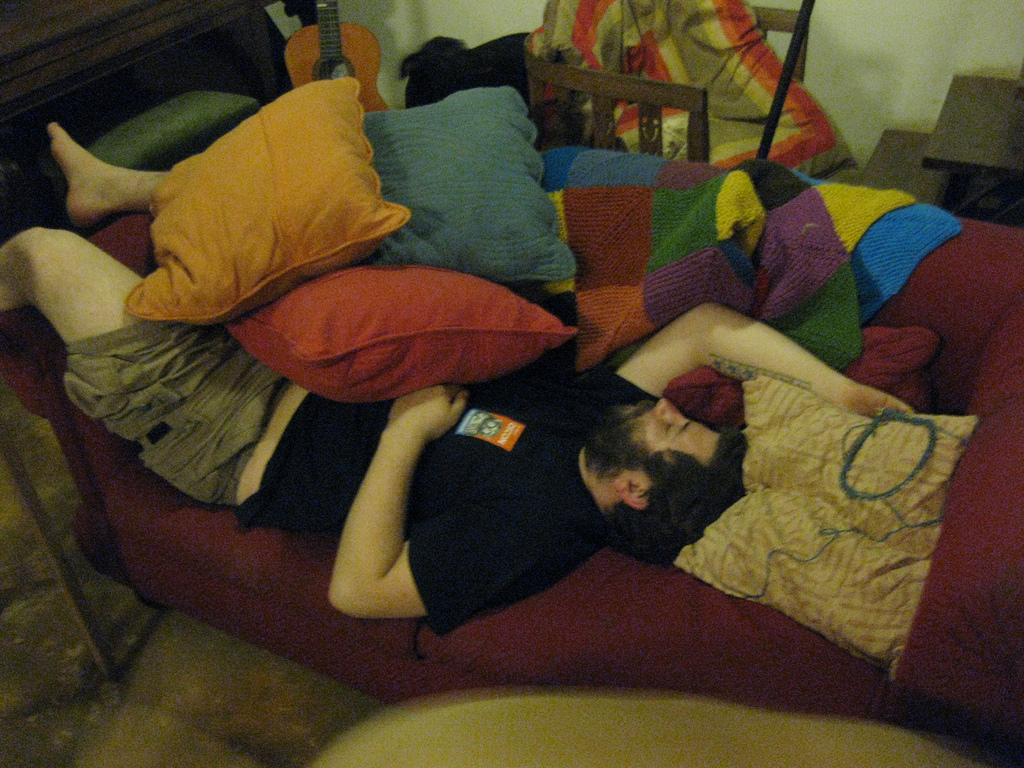 image of guy sleeping on couch with feet sticking out and lots of pillows